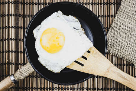 Fried egg on a wooden spatula over a frying pan.の写真素材
