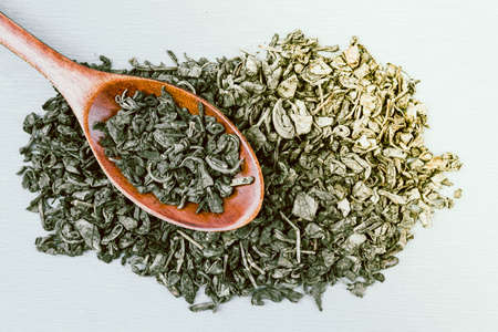 Green dry tea and wooden spoon on a light backgroundの写真素材