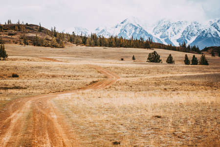 Beautiful view of the hills with a dirt road to the snowy peaks. Colorful mountain valley with rocks.の写真素材