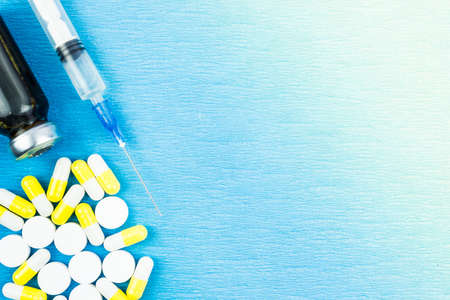 White and yellow pills and a syringe on a blue table. Place for text.の写真素材