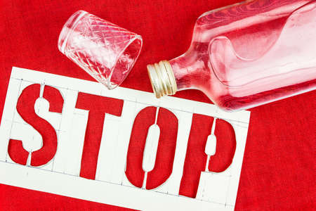 Stop sign, bottle and shot glass on the red tablecloth. The danger of alcoholism. Fight against excessive consumption of alcoholic beverages.の写真素材