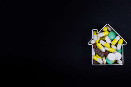 Tablets and capsules in the shape of a house on a dark background. Copy space for textの写真素材