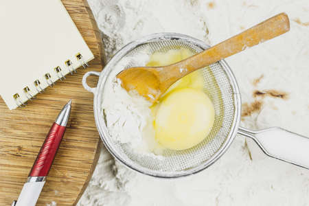 Notebook for recipes, egg, wooden spoon on a background of flour. Preparation of baking, kneading dough. Homemade meal made of flour.の写真素材