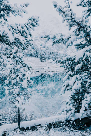 Snowfall on the mountain lake. Reflection of rocks and trees in the water surface. First snow in the mountains.の写真素材