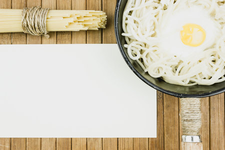 Pan with spaghetti and scrambled eggs on a wooden table. Bundle of dry spaghetti, the cooking. Copy...