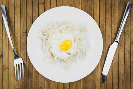 Scrambled eggs and spaghetti in plates, knives and fork on wooden table. Home-made dinner, lunch at the restaurant.の写真素材