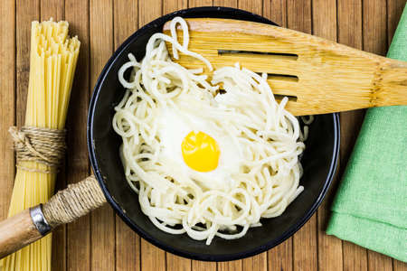 Fried egg and spaghetti in a black pan on a wooden table. Cooking at home, rustic food.の写真素材