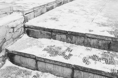 Dangerous stone staircase under the snow in winter. Ice in the city on the sidewalk.の写真素材