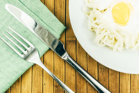 Egg and spaghetti in a white plate, fork on a green textile napkin. Dinner at restaurant. Lunch in an Italian cafe.の写真素材