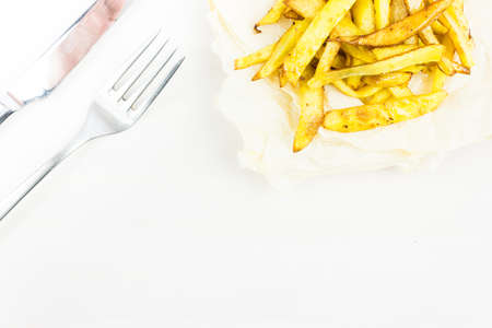 Pieces of fried French fries on a sheet of parchment and Cutlery on a wooden table. Copy space for textの写真素材