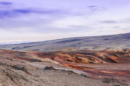 Pink clouds over mountain range. Rocks under snow on horizon. Sunset in mountain valleyの写真素材