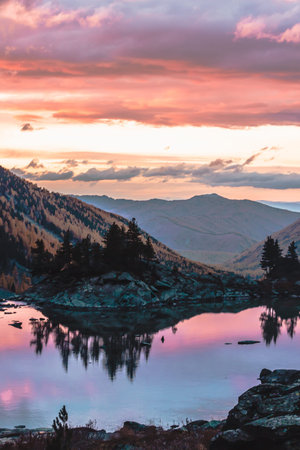 Dawn in mountain valley. Sunset with red clouds on lake between rocks