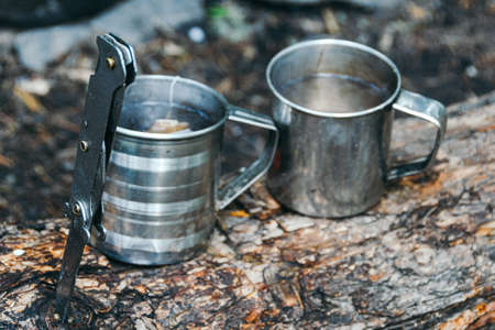 Two metal mugs on tree. Adventure in nature, tourism. Tea party in extreme conditions.の写真素材
