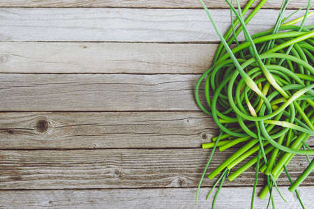 Green stalks of garlic on wooden table. The twisted stems of plants from seed. Preparation of summer salad for healthy dietの写真素材