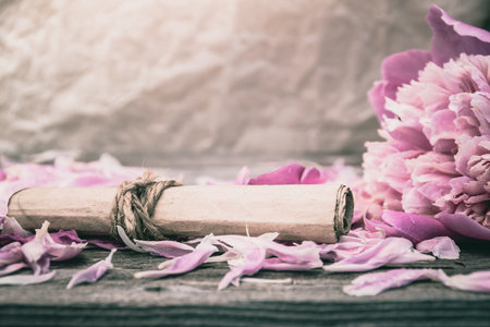 Roll of old paper on rose petals. Love letter, a wedding invitation. Romantic atmosphere of ...