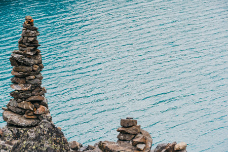 Neat pile of stones for tourists on shore of turquoise lake. Stone mound on shore of sea