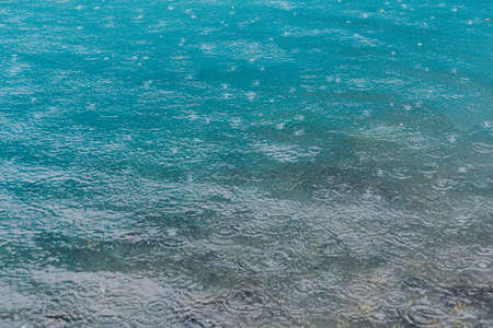 Raindrops on water surface of lake. The turquoise water of river. Rainy weather at seaの写真素材