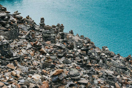 Pile of stones for tourists on shore of blue lake. Sea rocky shore on summer day. Meditation on natureの写真素材