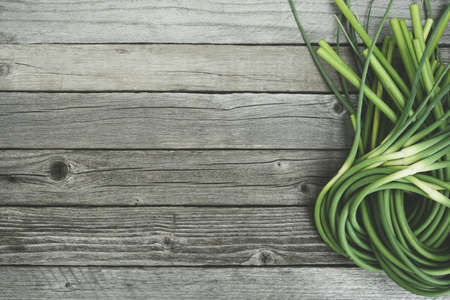 Green stalks of garlic on wooden table. The twisted stems of plants from seed. Preparation of summer salad for healthy dietの写真素材