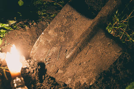 dirty old shovel in dark trench. Digging grave by candlelight. Mystical night sceneの写真素材