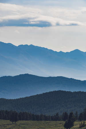 Hills in blue haze on horizon. Silhouettes of mountains in valley at sunsetの写真素材