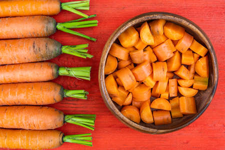 freshly cut carrot slices in plate on red wooden table, cooking vegetarian salad for healthy eatingの写真素材