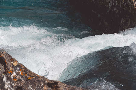 rocky shore of sea, fast river in mountain valley, ocean surf on summer dayの写真素材