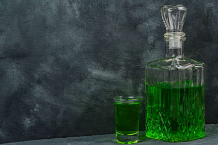 Glass shot and bottle of absinthe in carafe on table of bar. Alcohol consumption in restaurant, alcoholism in urban society. Green cocktail for partyの写真素材