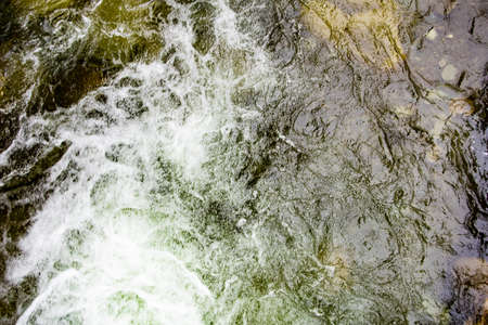 Turbulent spring stream of mountain river. Water foams, breaks into splashes on stones. Power of nature, continuous movement and energy.の写真素材