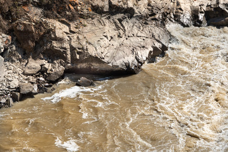 Muddy stream in mountain canyon. Yellow dirty river after flooding in early spring. Dry sheer cliffs...