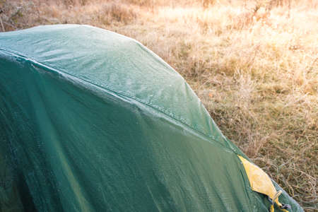 Roof of tourist tent under the morning sun. Green waterproof fabric was covered with cold and condensation from frost. Equipment for survival in the wildの写真素材