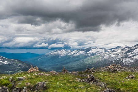 View of mountain valley with snowy ridge on horizon. Forest and glacier on slope, in blue sky cumulus clouds. Concept of untouched nature, hiking trip to highlands.の写真素材