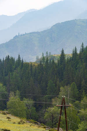 Wooden poles with electrical wires in mountainous region. Spread of electricity to hard-to-reach areas. Old electrification technologies of last centuryの写真素材