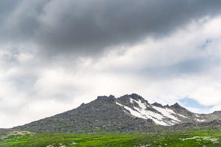 Mountain range with glaciers on slope under gloomy sky. Rainy gray clouds over snowy cliffs. Planning climb to top. Achieving lofty goal, hiking through stone valleyの写真素材