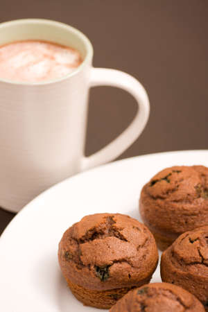 Frehsly baked muffins on a white serving plate and hot chocolate in a white cupの写真素材