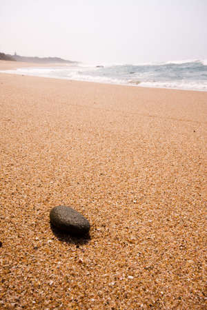 A single black rock lying on the beach with waves in the の写真素材