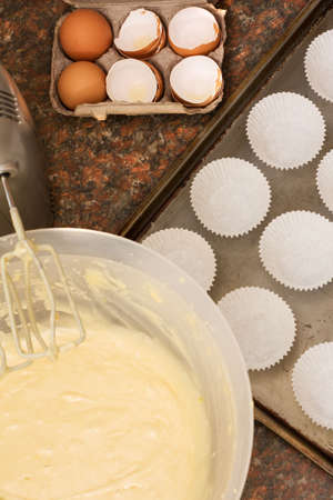 Kitchen utensils, ingredient and cake batter in bowl next to a baking tray lined with cup cake paper cupsの写真素材