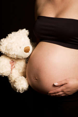 Young pregnant Caucasian woman holding teddy bear against her bare bellyの写真素材