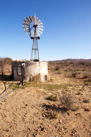 Wind blown windpump pumping water next to dam in Karooの写真素材