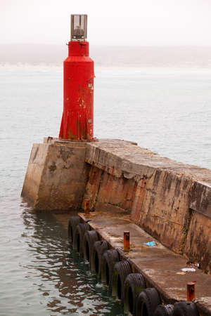Single bright red lighthouse on pier in harbor, misty weatherの写真素材