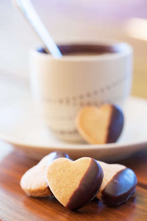 Chocolate dipped heart shaped cookies and cup of coffee on wooden tableの写真素材