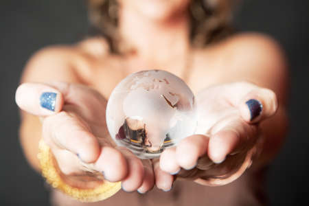 Young Caucasian woman holding glass world orb in her hands against dark background, selective focus の写真素材
