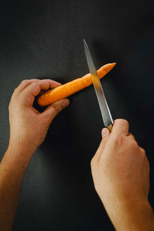Hands cutting a carrot with a knifeの写真素材