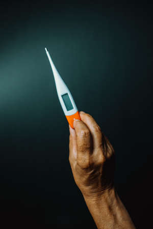 Old hand grabbing a thermometer over a dark backgroundの写真素材