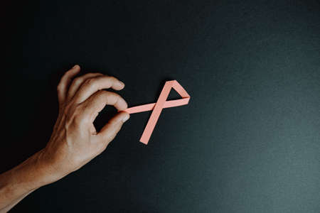 An old hand grabbing a pink ribbon over a dark backgroundの写真素材