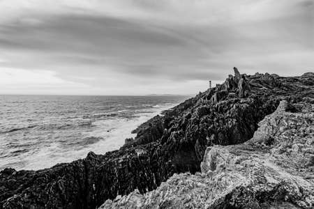 Black and white dramatic shot of the lighthouse on the broken coast of Galiciaの写真素材