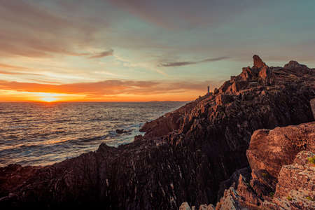 Dramatic horizontal shot of a white lighthouse during the sunset from the rocks of the coastの写真素材