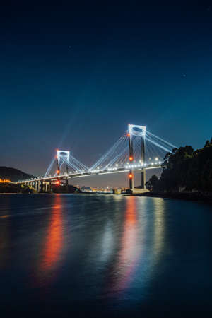 Luminous bridge reflecting in the water at nightの写真素材