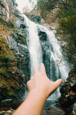 An out of focus hand reaching to a majestic waterfallの写真素材