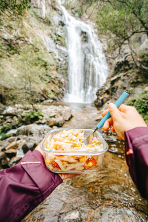 A point of view shot of a female hiker eating in front of a waterfallの写真素材